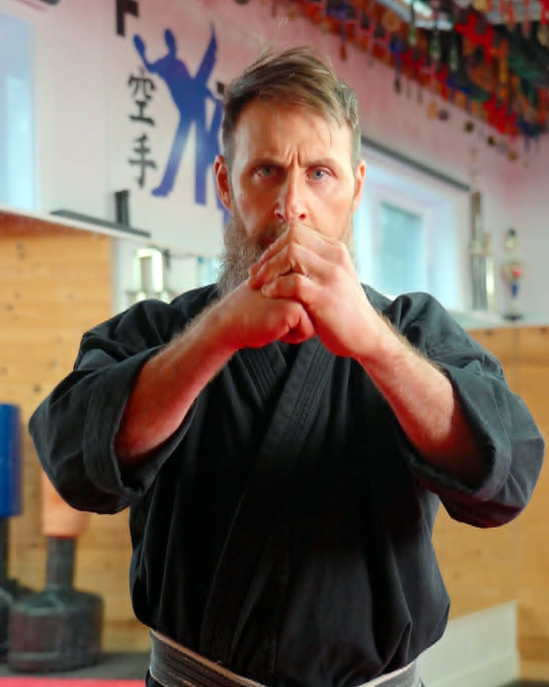 José Vinciarelli, senseï en chef, en karatégi noir, fait le salut du Kenpo au dojo, devant le logo K2V et les médailles